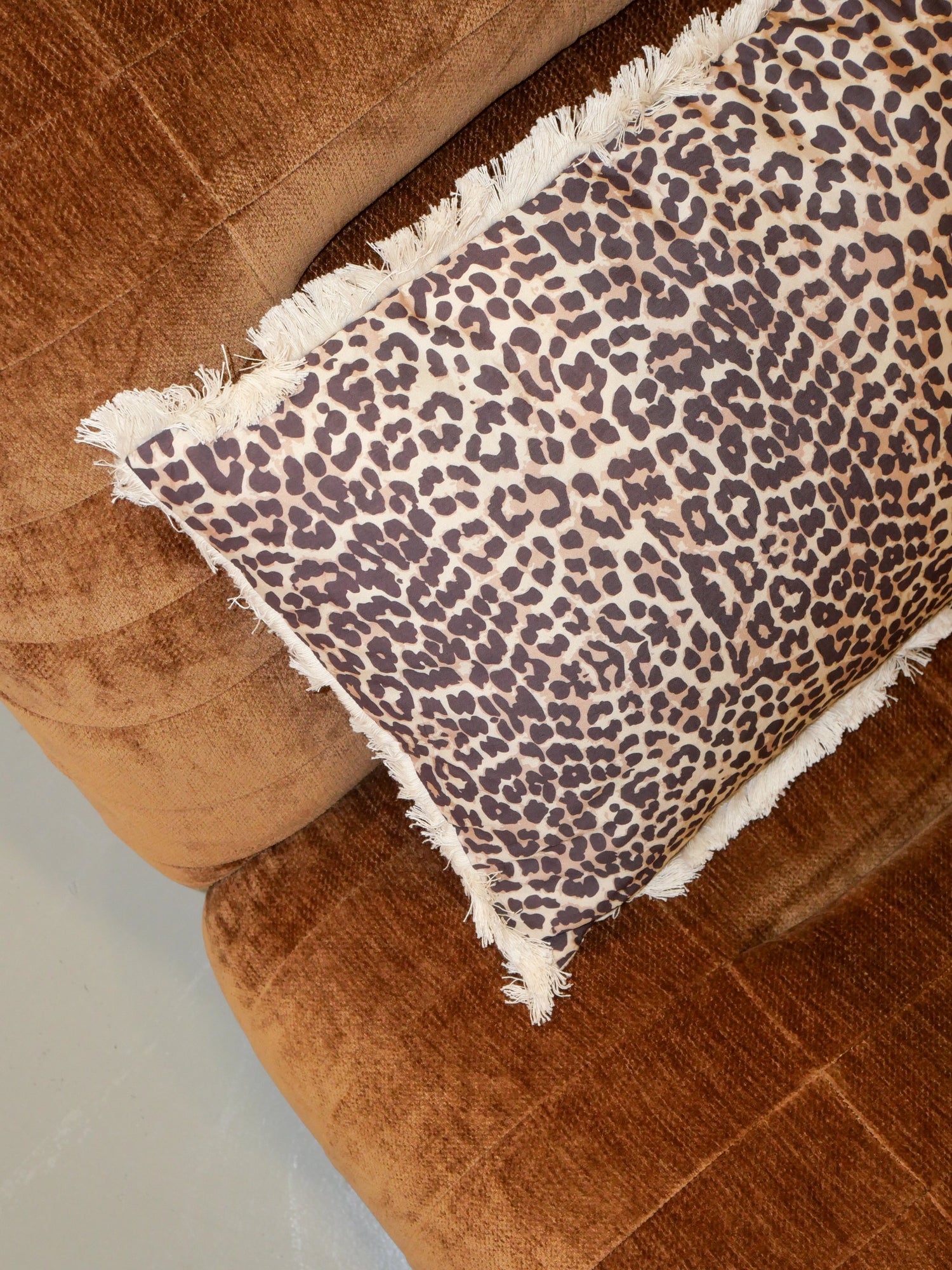 Soft velvet sofa in a warm brown tone with a decorative leopard print cushion featuring fringed edges, photographed from above.