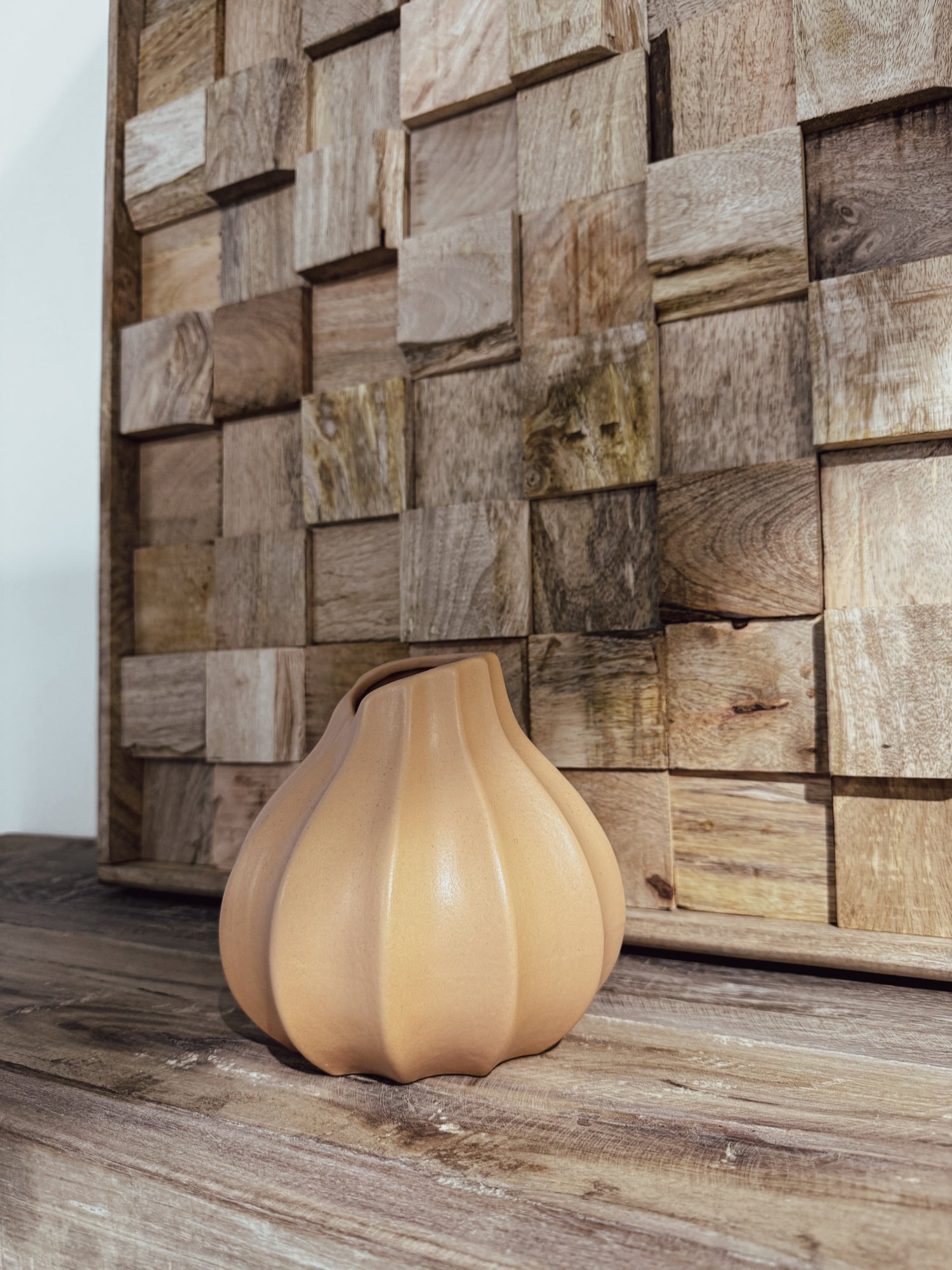 Smiling model holding a ceramic vase with a wavy shape, styled in an industrial space with exposed brick walls and large windows.